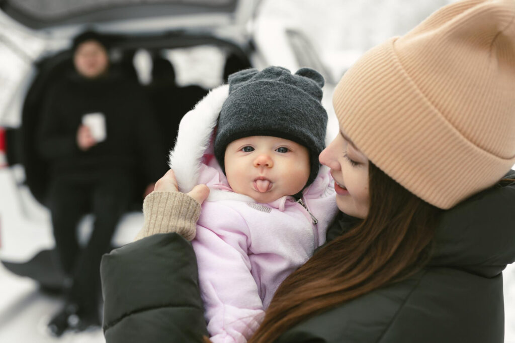 baby girl looks into camera shows her tongue her mothers arms winter