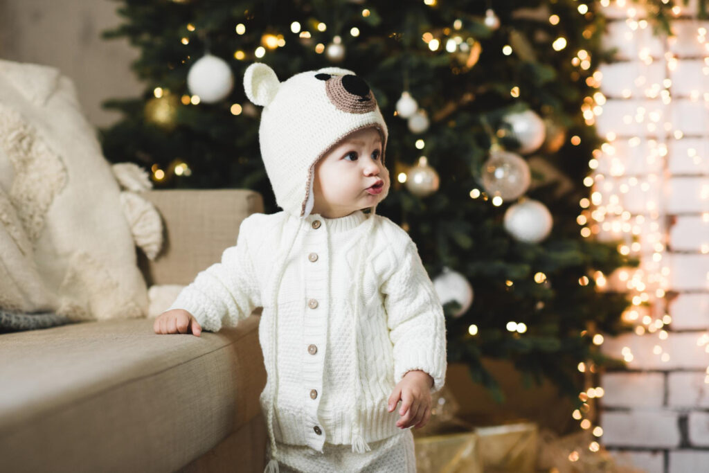 cute baby girl wearing knitted suit hat posing christmas tree