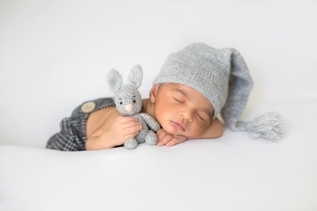 little infant sleeping with cute grey hat with toy rabbit his hands